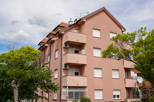 Ponuda nekretnina View of a pink residential building surrounded by lush greenery in Zagreb, Croatia.